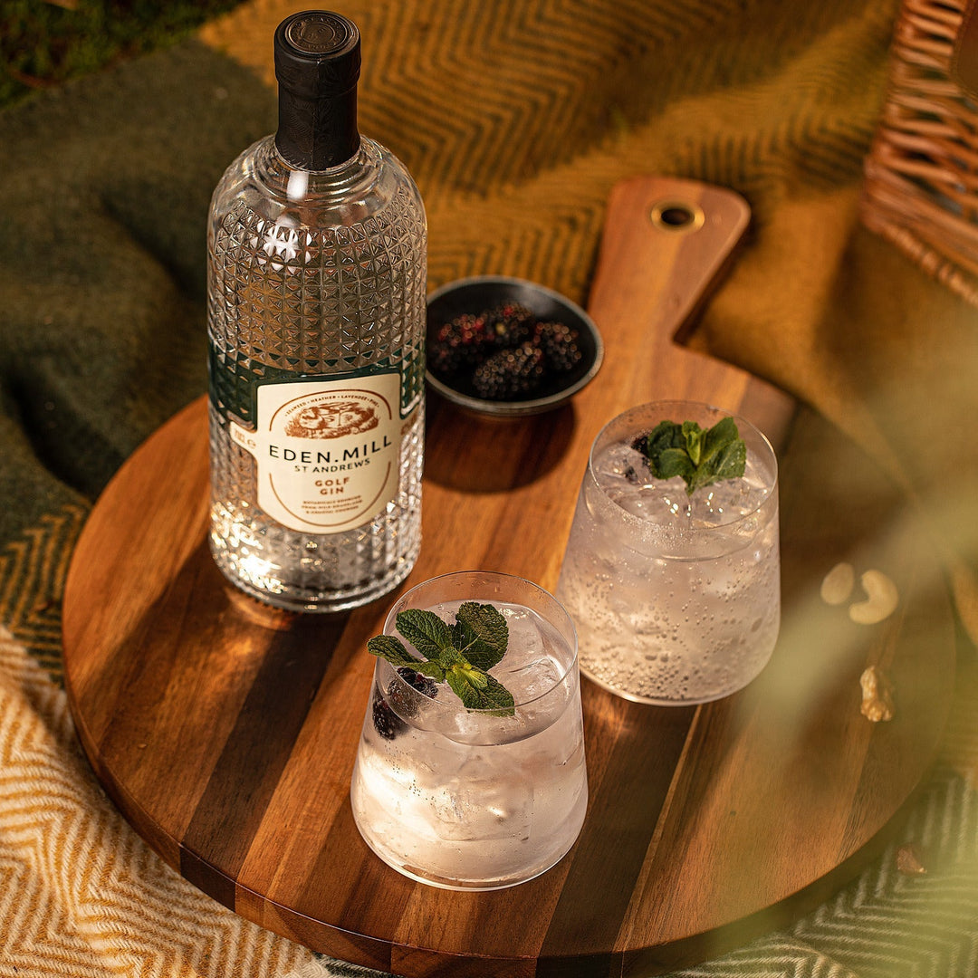 Bottle of Golf Gin on wooden board from above with two gin and tonic drinks and bowl of berries